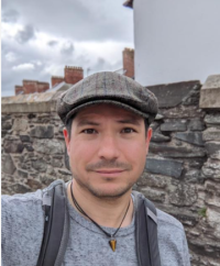 Francois standing in front of a stone wall; with a hat on, looking at the camera